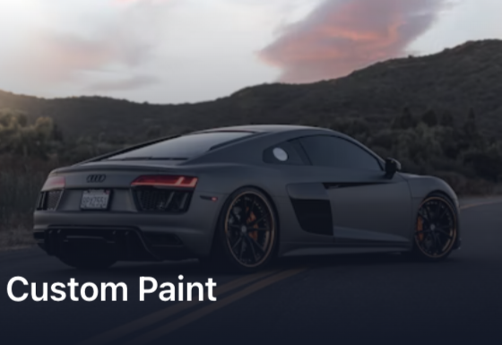 Sleek gray sports car with custom paint driving on a winding road at sunset.